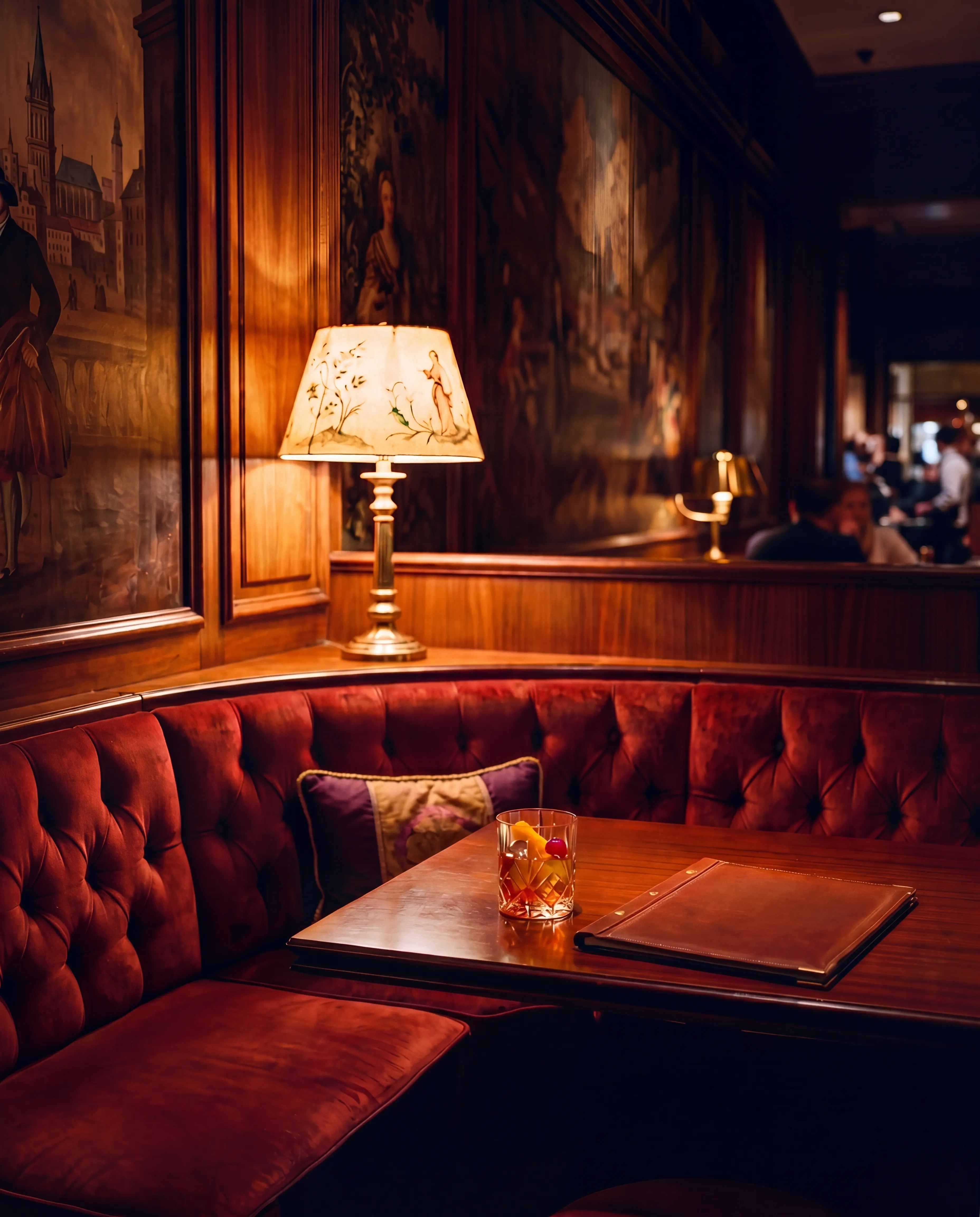 corner booth at 10pm — velvet banquette, brass candlestick, lamp.
